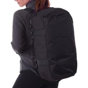 A black duffle bag is being worn on the back of a person in a grey jacket. The bag features a logo.
