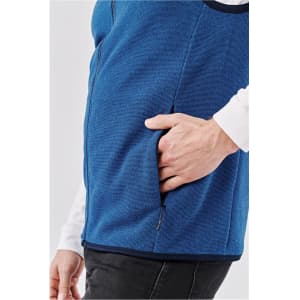 A blue vest featuring a side pocket, worn over a white long-sleeve shirt. It has a sleek design and casual style.