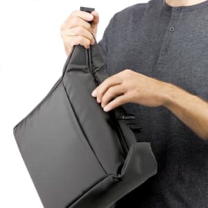 A person holding a dark grey cooler bag with a zippered opening and a shoulder strap.