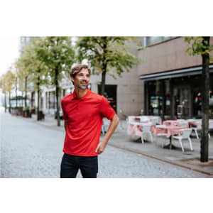 A red polo shirt worn by a man standing on a city street, surrounded by trees and outdoor seating.