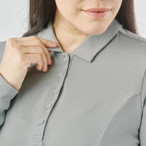 A close-up of a woman adjusting the collar of a grey long-sleeve polo shirt with buttons and a logo.