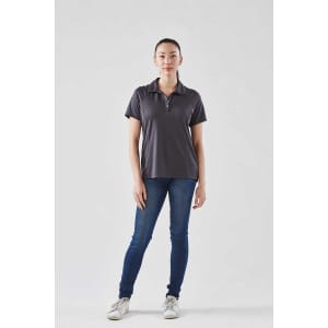 A grey women's polo shirt displayed on a model, paired with blue jeans and white sneakers.