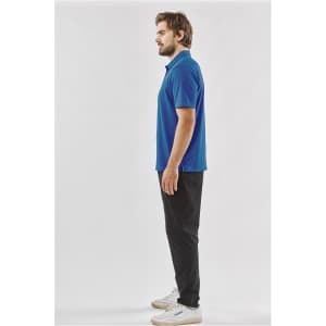 A side view of a man wearing a blue polo shirt and black trousers, with a logo on the shirt.
