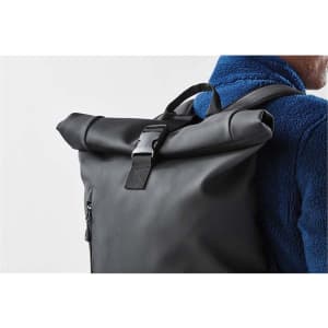 A black roll-top backpack with adjustable straps and a buckle fastening, worn on a person's back.