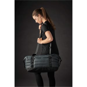A grey quilted duffle bag with adjustable straps, being carried by a person in athletic wear.