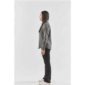 A side view of a woman wearing a grey button-up shirt and black pants, standing with a neutral expression.