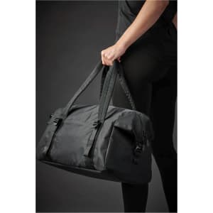 A person holds a black duffle bag with braided handles, featuring buckles and a sleek design.