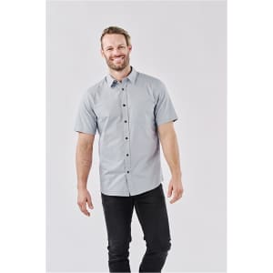 A man wearing a short-sleeved, light blue button-up shirt with a chest pocket and a logo.