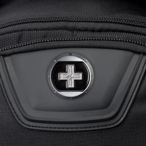 A close-up of a black backpack featuring a round logo on a zippered pocket.