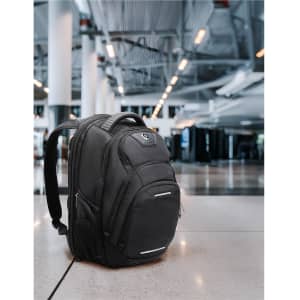 A black Swissdigital Stealth Neptune backpack with pockets and a logo, positioned in an airport setting.
