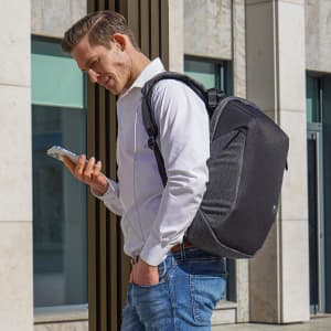 A man wearing a grey Swissdigital Cosmo 3.0 backpack checks his phone outdoors. The backpack features a logo.