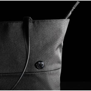 A black tote bag with a structured design and a sleek shoulder strap, featuring a circular logo.