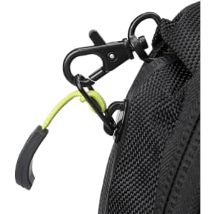 A close-up of a black backpack with a green accent on the zipper pull and a metal clip.