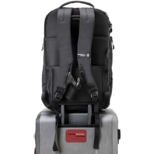 A black backpack with padded straps sits atop a silver suitcase, featuring a branding logo on the front.