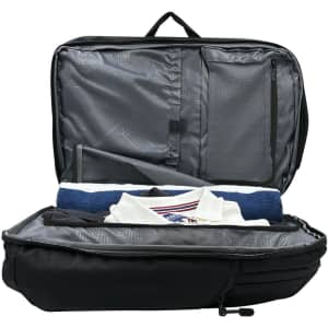 A black backpack with an open interior, featuring grey lining and neatly arranged items including a towel and a shirt.