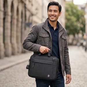 A man holding a black laptop sleeve, featuring a handle, standing on a cobblestone street. The product has a logo.