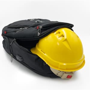 A black backpack partially unzipped, revealing a yellow hard hat inside. The backpack features zippers and a logo.