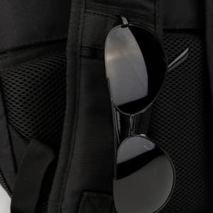 A black backpack with a mesh pocket and a pair of black sunglasses hanging from it. It features a logo.