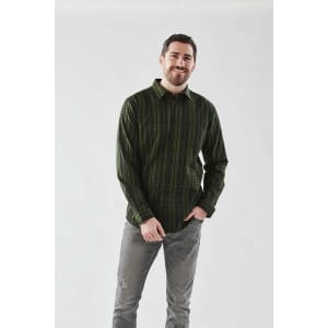 A man in a green checkered button-up shirt with long sleeves stands against a plain background, smiling.