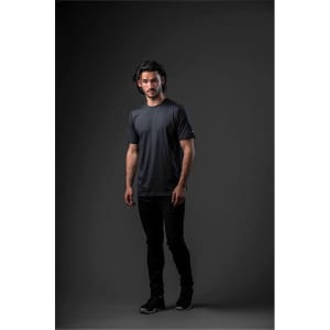 A model wearing a black short-sleeve t-shirt, standing against a dark background. The shirt has a logo.