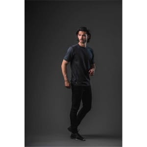 A model wearing a short-sleeve men's T-shirt in dark grey, standing against a black background. The shirt features a logo.