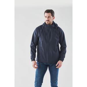 A man is wearing a navy lightweight rain jacket, featuring a hood and a logo on the chest.