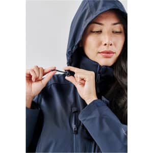 A woman adjusts the fastening on a navy lightweight rain jacket with a hood, featuring a logo on the sleeve.