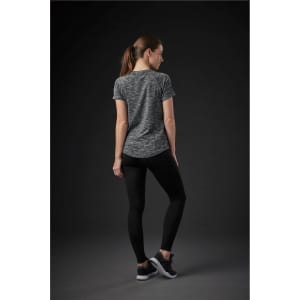 A woman is wearing a grey patterned short-sleeve T-shirt, paired with black leggings and sneakers. The back view is displayed.