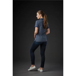 A woman in a navy and white striped polo shirt stands with her back to the camera, paired with dark jeans and white shoes.
