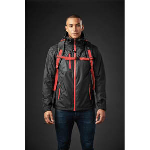 A man wearing a black jacket with red straps and a backpack. The background is dark.