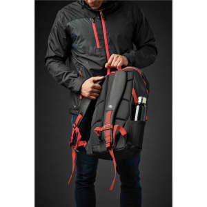 A black and red backpack is held by a person wearing a black jacket, featuring a side pocket for a drink bottle.