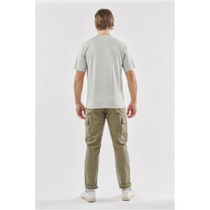 A man wearing a light grey T-shirt and khaki pants, standing with his back to the camera. The shirt features a logo.