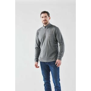 A man wearing a grey 1/4 zip pullover, paired with blue jeans, against a light background. The pullover has a pocket and branding.