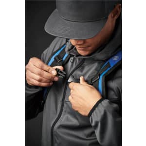 A person fastening a strap on a black backpack with blue accents while wearing a grey jacket and cap.
