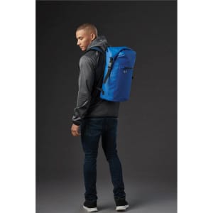 A man wearing a grey hoodie carries a blue Cirrus Backpack on his back. The backpack features a logo.