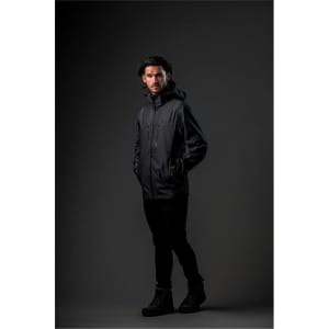 A model wearing a black Men's Patrol Softshell jacket, standing against a dark background. The jacket features a hood and has branding.