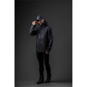 A man wearing a black Men's Patrol Softshell jacket and cap, standing against a dark background. The jacket has a logo.