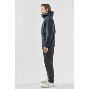 A navy blue technical shell jacket with a hood, featuring a logo, worn by a person standing sideways.