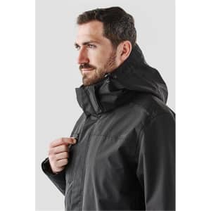 A man wearing a black Magellan System jacket, featuring a hood and front zipper, with a logo visible.