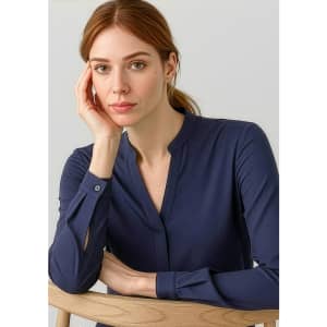 A woman poses wearing a navy long sleeve blouse with a button-up neckline, sitting against a light background.
