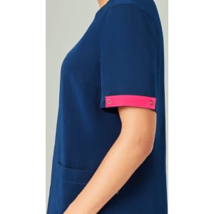 Unisex navy scrub top with pink accents on the sleeves, featuring a side pocket and a circular logo detail.