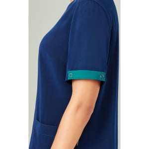 A unisex navy scrub top with short sleeves featuring teal cuff detailing and a front pocket.