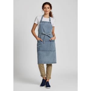 A denim apron in blue, worn by a model over a white t-shirt, featuring pockets and a tied waist.