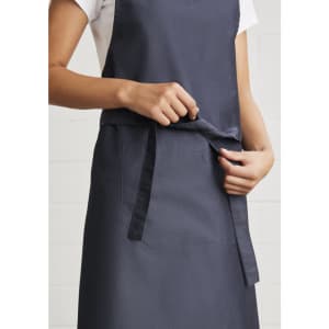 A navy blue Urban Bib Apron featuring a front pocket and adjustable tie at the waist, with branding visible.