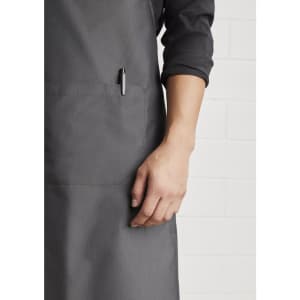 A grey Urban Bib Apron featuring a pocket and a pen holder, highlighting its practical design.