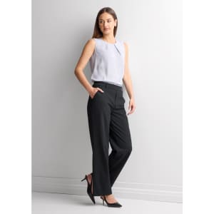 A woman stands wearing soft stretch pants in black, paired with a light grey sleeveless top and black heels.