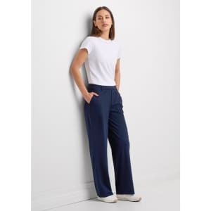 A woman stands against a wall wearing navy blue soft stretch pants and a fitted white t-shirt, with pockets visible.