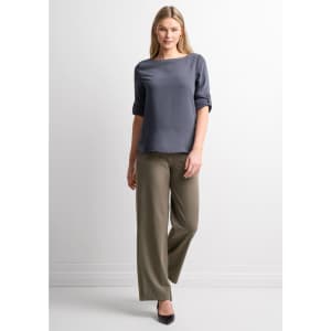 A woman wearing a grey top and olive green soft stretch pants, standing against a light background.