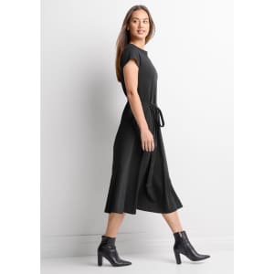 A black midi dress with short sleeves and a waist tie, paired with stylish ankle boots. It features a subtle logo.