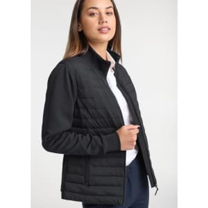 A women's tailor jacket in black, featuring a quilted design and a zip closure. A model is wearing it with a white shirt.